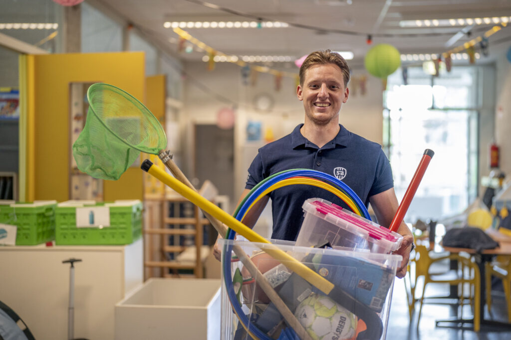 Buurtsportcoach met allerlei sportmateriaal in zijn handen